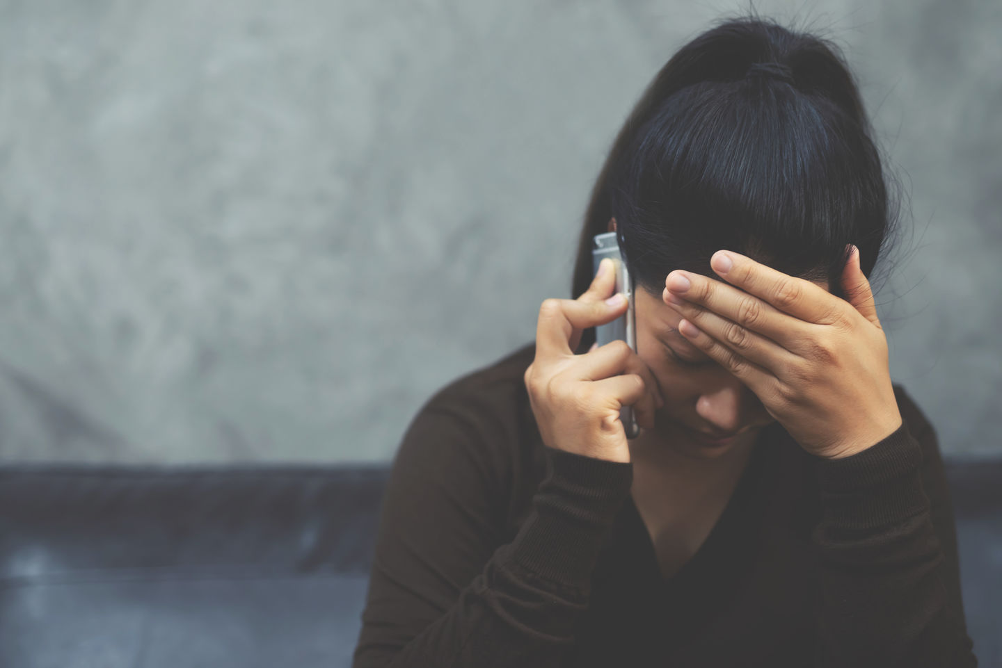 Eine Frau mit Pferdeschwanz telefoniert mit dem Handy, hält sich dabei die Hand vor die Stirn und blickt zu Boden. Foto: © Rattankun Thongbun/Getty Images/iStockphoto